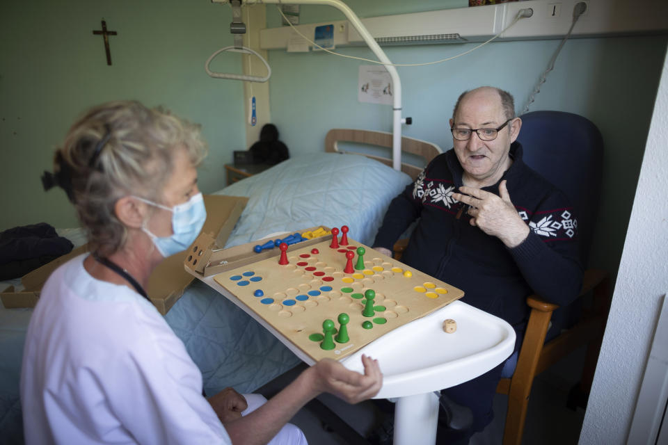 Gilbert Beck plays a board game with an activity leader inside his room at a nursing home in Ammerschwir, France Thursday April 16, 2020. (AP Photo/Jean-Francois Badias)