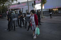 Two neighbours of restricted mobility areas in Madrid due to the coronavirus outbreak cross the street in front an anti-riot police unit short after a residents protest demanding more resources for public health system and against social inequality in the southern neighbourhood of Vallecas, Madrid, Spain, Thursday, Sept. 24, 2020. The regional government is set to announce Friday new restrictions in Madrid, where gatherings are limited to a maximum of 6 people and more than 850,000 residents have been partially locked down this week. (AP Photo/Bernat Armangue)