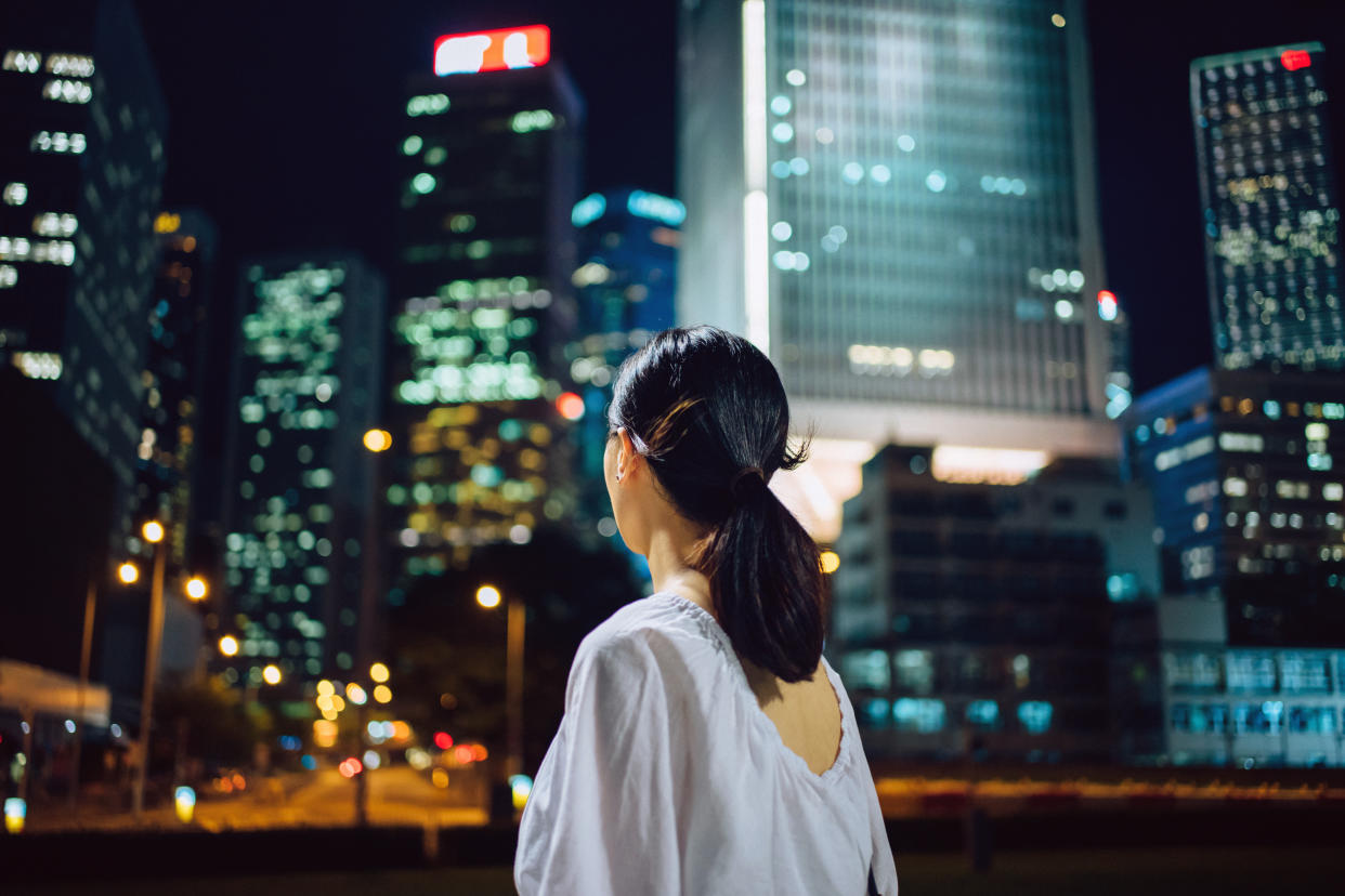 Rear view of young woman looking towards illuminated city skyline in central business district