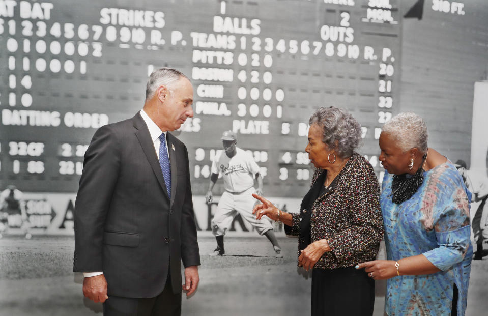 Major League Baseball Commissioner Rob Manfred, left, Rachel Robinson, center, widow of the late Jackie Robinson, and Sharon Robinson, the couple's daughter, inspect a mural-sized photograph of Jackie Robinson in uniform displayed at the Museum of the City of New York Thursday, Jan. 31, 2019, in New York. The photo is part of "In the Dugout with Jackie Robinson," an exhibition celebrating Robinson's 100th birthday, mounted in collaboration with The Jackie Robinson Foundation. The exhibit features 30 photographs originally shot for Look Magazine (most never published) and rare Robinson family home movies plus memorabilia related to Robinson's career. (AP Photo/Kathy Willens)