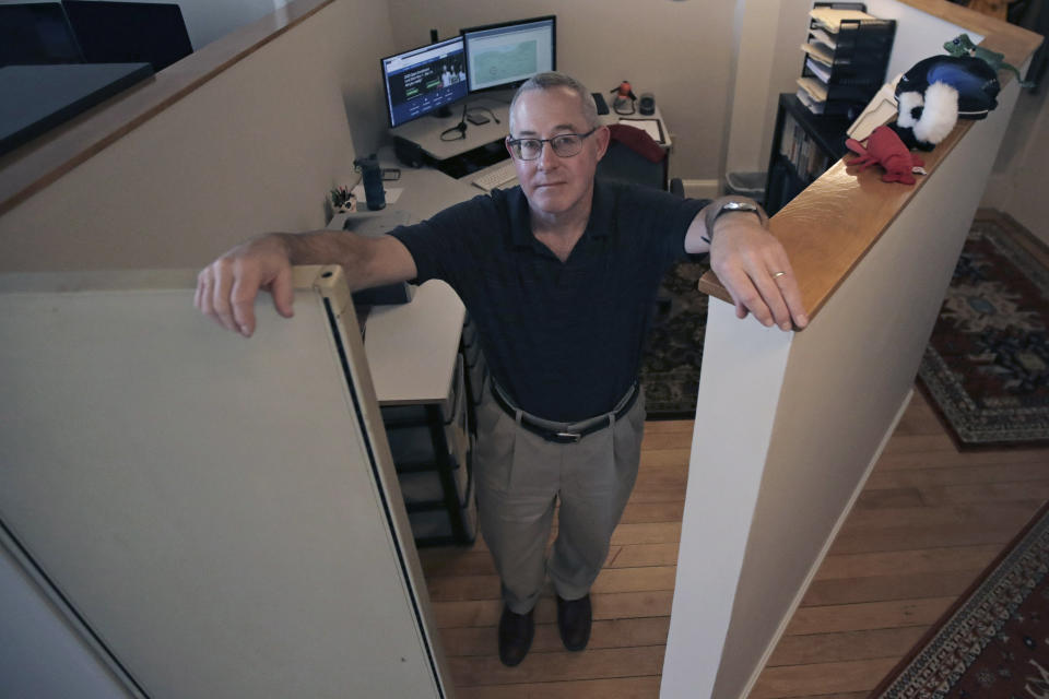 John Gold, self-employed graphics designer, poses in his shared office cubical in Portland, Maine, Wednesday, Oct. 23, 2019. Gold has been covered by the Affordable Care Act since it started, and plans on signing up again when the enrollment season starts Nov. 1. The 2020 sign-up season for the Affordable Care Act is getting underway with premiums down slightly in many states and more health plan choices for consumers. (AP Photo/Charles Krupa)