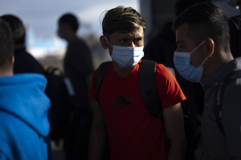 Migrants stand in groups as they arrive at a bus stop after leaving a processing facility, Friday, Feb. 23, 2024, in San Diego. Hundreds of migrants were dropped off Friday at a sidewalk bus stop amid office parks in San Diego with notices to appear in immigration court after local government funding for a reception center ran out of money sooner than expected. (AP Photo/Gregory Bull)