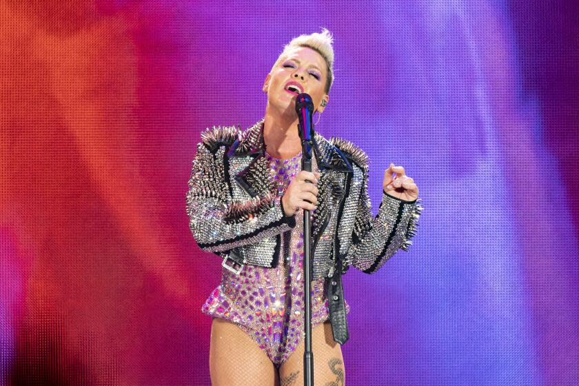 Pink in her signature updo with a studded and bejeweled leather jacket and pink body suit holding a microphone