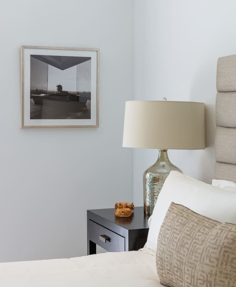 Detail of bedroom with pale gray walls, warm gray fabric headboard