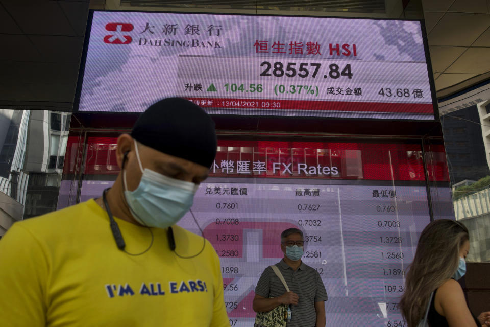People wearing face masks walk past a bank's electronic board showing the Hong Kong share index at Hong Kong Stock Exchange in Hong Kong Tuesday, April 13, 2021. Asian shares were mostly higher on Tuesday with hopes growing for a global economic rebound despite worries over renewed surges in coronavirus cases. (AP Photo/Vincent Yu)