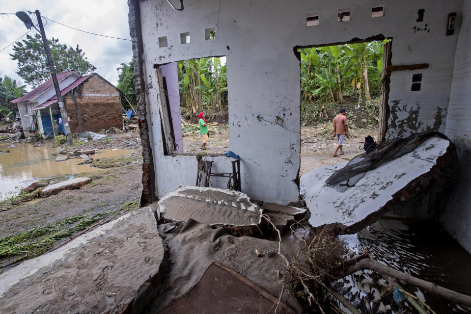 People are seen through the ruins of a house at a neighborhood affected by a flood in Medan, North Sumatra, Indonesia, Friday, Dec. 4, 2020. Torrential rains in the country's third largest city swelled rivers and flooded thousands of homes leaving a number of people killed and missing. (AP Photo/Binsar Bakkara)