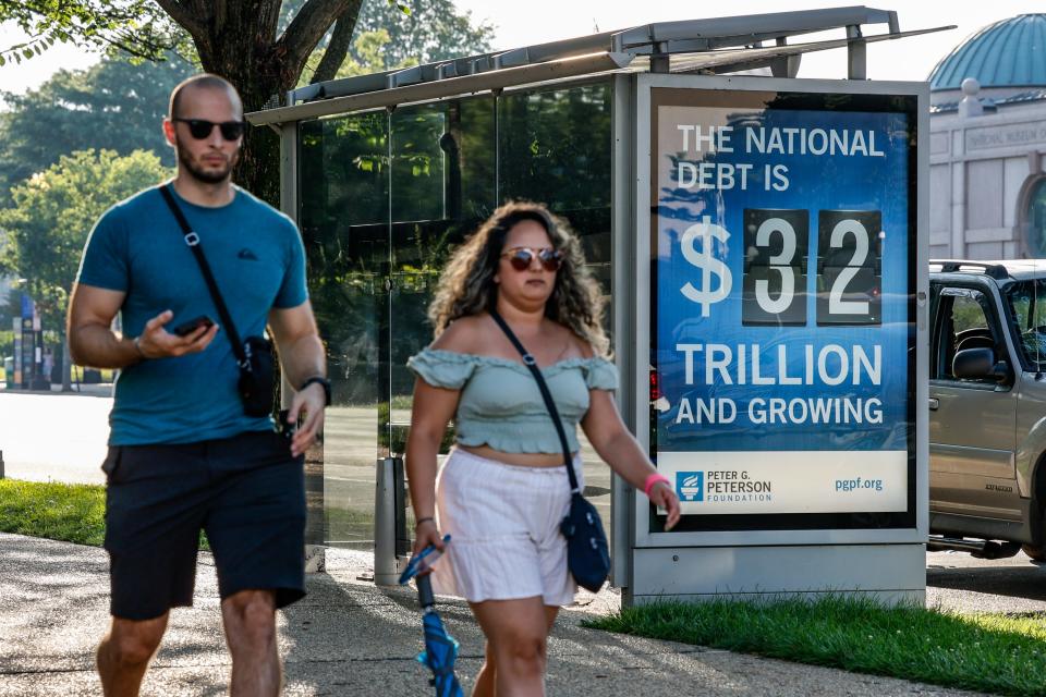 Pedestrians walk past a poster and electronic billboard displayed at Independence Ave and 9th St's SW that displays the U.S. National debt per person and as a nation at $32 trillion on July 06, 2023, in Washington, D.C.