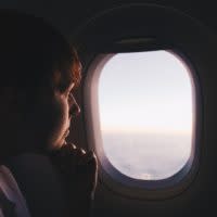 Ein Mann in einem Flugzeug schaut gedankenverloren aus dem Fenster mit Sonnenblende.