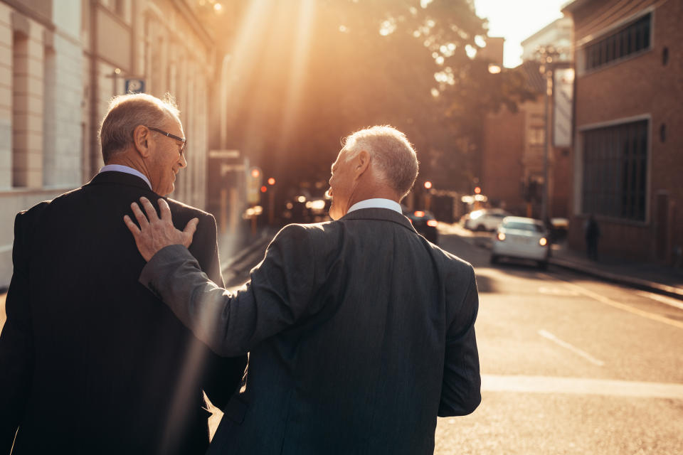 Rear view of two business people walking outdoors and talking next to an office building after a successful business meeting. Senior business professionals walking together on a sunny day.