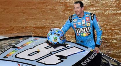 Kyle Busch smiles for the crowd beside the No. 18 Toyota after winning on Bristol Motor Speedway\