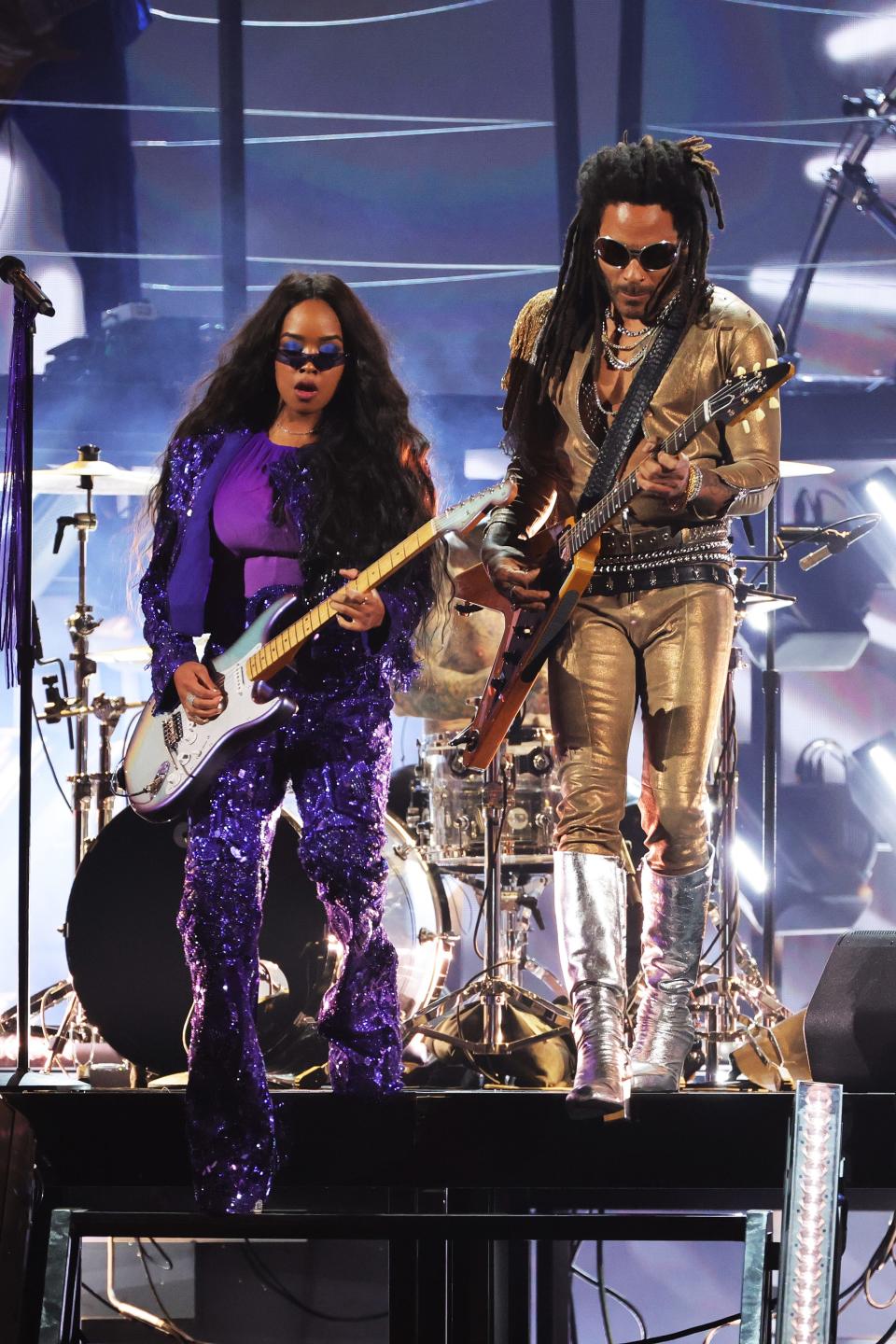 H.E.R. in a purple fringe pant costume and Lenny in a gold jumpsuit with black studded belts and silver knee-high platform boots.