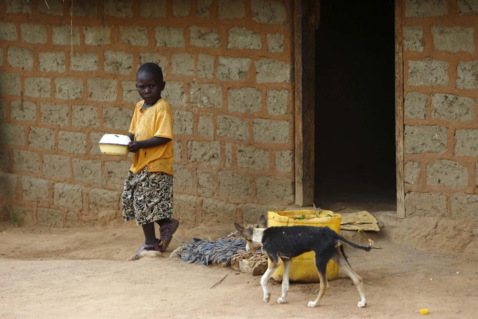 Otra imagen del hijo de Patrick Kasamu, en esta ocasión llevando su almuerzo en las manos junto a un perro en la visita de los cuidadores a Chikonga.