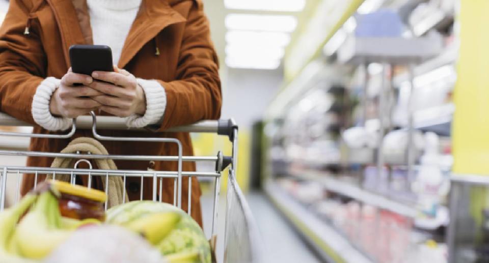 Woman pushing grocery trolley holding phone