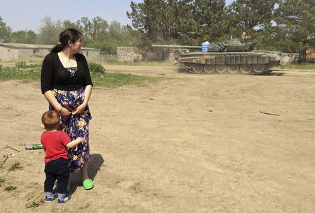 A woman with a boy looks at a tank as it drives through the settlement Khutor Chkalova on its way to the Russian military training ground 'Kuzminsky' near the Russian-Ukrainian border in the Rostov region, Russia, May 26, 2015. REUTERS/Maria Tsvetkova