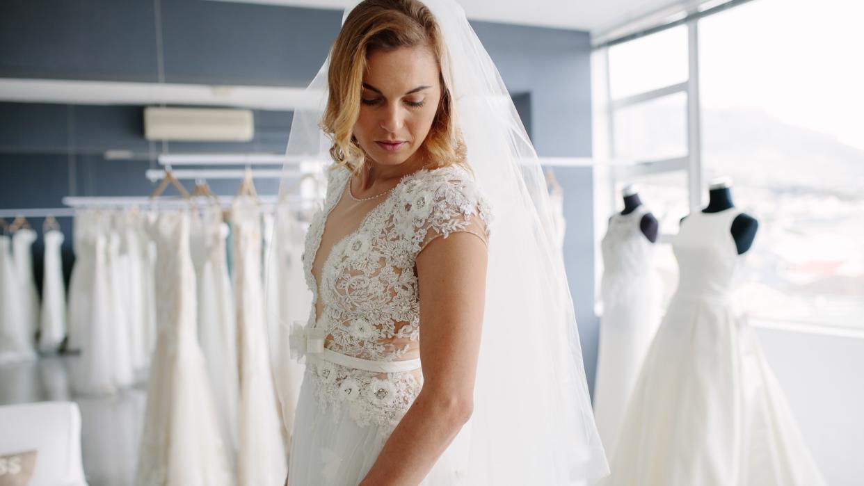 Beautiful young woman trying on bridal gown in wedding fashion shop.