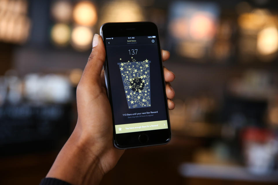 A person holds up a phine showing Rewards in the Starbucks app.