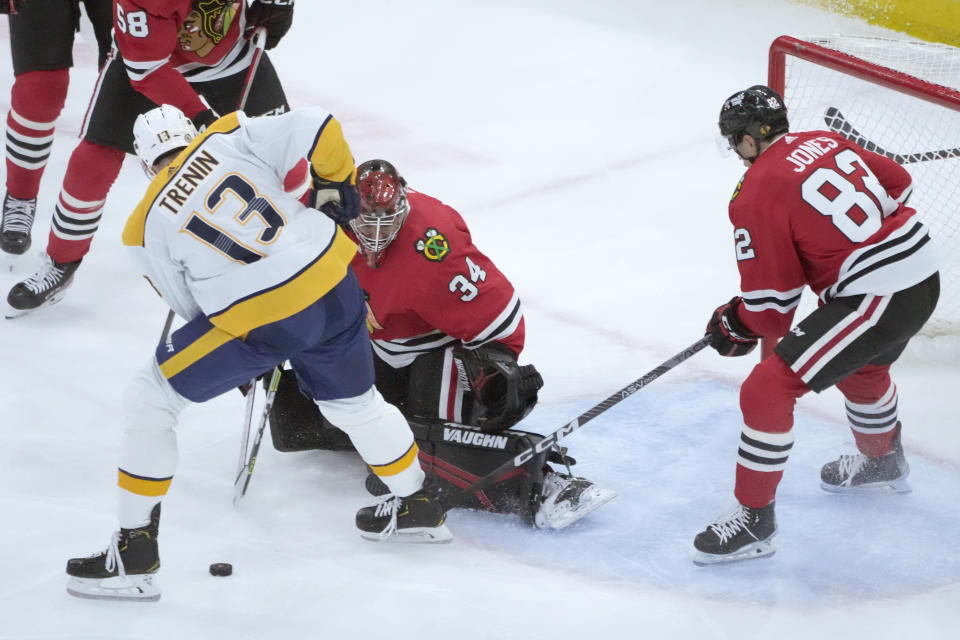 Chicago Blackhawks' Petr Mrazek (34) makes a save on a shot by Nashville Predators' Yakov Trenin (13) as Blackhawks' Caleb Jones also defends during the first period of an NHL hockey game Saturday, March 4, 2023, in Chicago. (AP Photo/Charles Rex Arbogast)