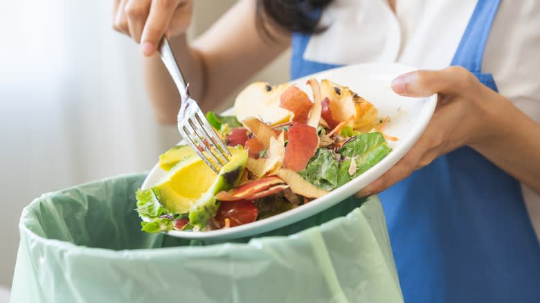 person scraping food into trash