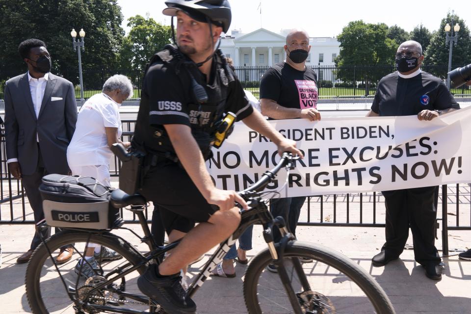 A U.S. Secret Service officer rides his bicycle past protesters, including Ben Jealous, center, and Rev. Melvin Wilson, right, as they rally for voting rights, Tuesday, Aug. 24, 2021, near the White House in Washington. (AP Photo/Jacquelyn Martin)