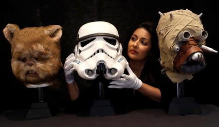 An employee of Prop Store poses for a photograph with an Ewok mask, a Stormtroopers' helmet and a prototype of a Tusken Raider mask at a preview of a film and tv memorabilia sale in London