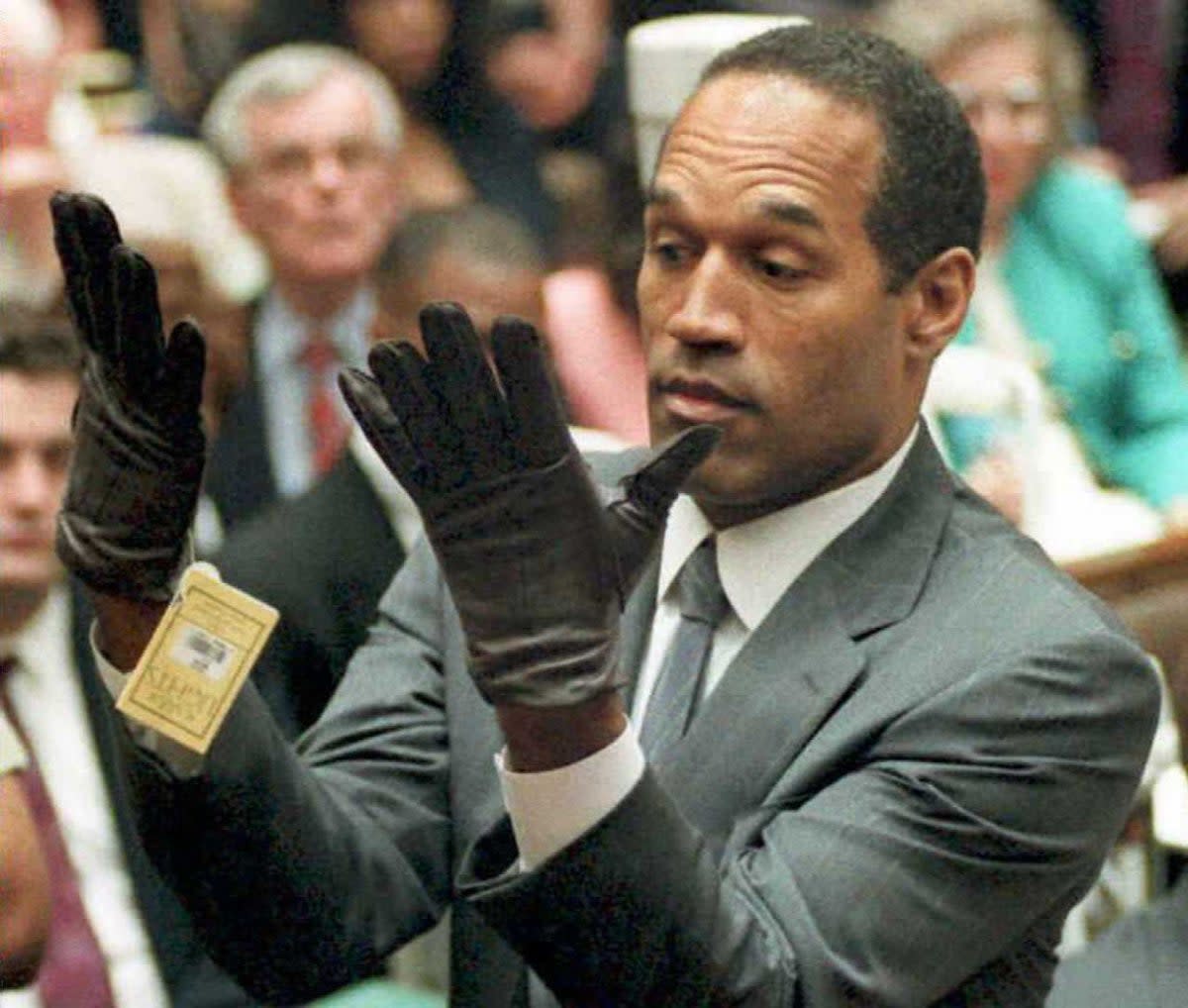 OJ Simpson looks at a new pair of Aris extra-large gloves that prosecutors had him put on 21 June 1995 during his double-murder trial in Los Angeles. (AFP via Getty Images)