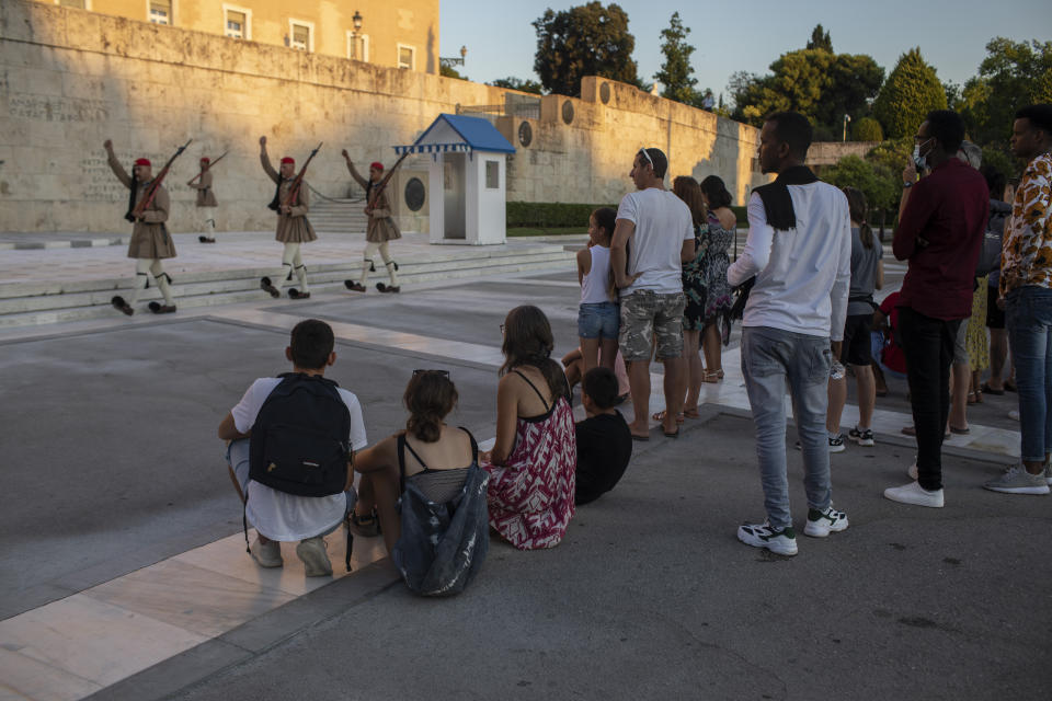 Tourists look at the changing of presidential guards ceremony outside the Greek parliament , in Athens, on Friday, July 31, 2020. Greek authorities introduced tougher restrictions this week following an increase in infections, most unrelated to tourism. (AP Photo/Petros Giannakouris)