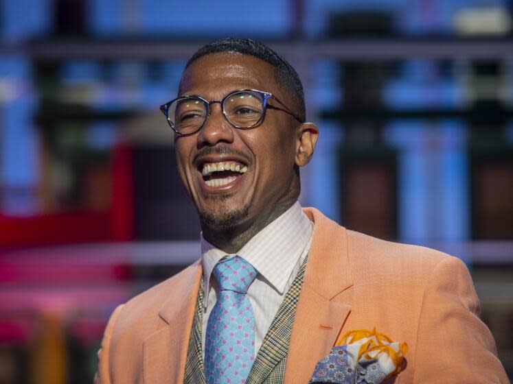 A man with glasses and a burnt orange suit laughs