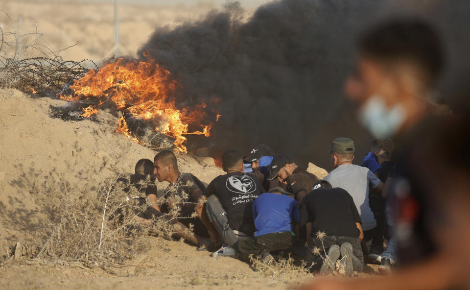 Protesters take cover next to tires on fire near the fence of Gaza Strip border with Israel during a protest east of Khan Younis, southern Gaza Strip, Wednesday, Aug. 25, 2021. Hundreds of Palestinians on Wednesday demonstrated near the Israeli border in the southern Gaza Strip, calling on Israel to ease a crippling blockade days after a similar gathering ended in deadly clashes with the Israeli army. (AP Photo/Abdel Kareem Hana)