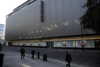 People wearing face masks walk past the Debenhams flagship department store on a side street off Oxford Street, during England's second coronavirus lockdown in London, Tuesday, Dec. 1, 2020. In another dark day for the British retailing industry, Debenhams said Tuesday it will start liquidating its business after a potential buyer of the company pulled out, a move that looks like it will cost 12,000 workers their jobs. (AP Photo/Matt Dunham)