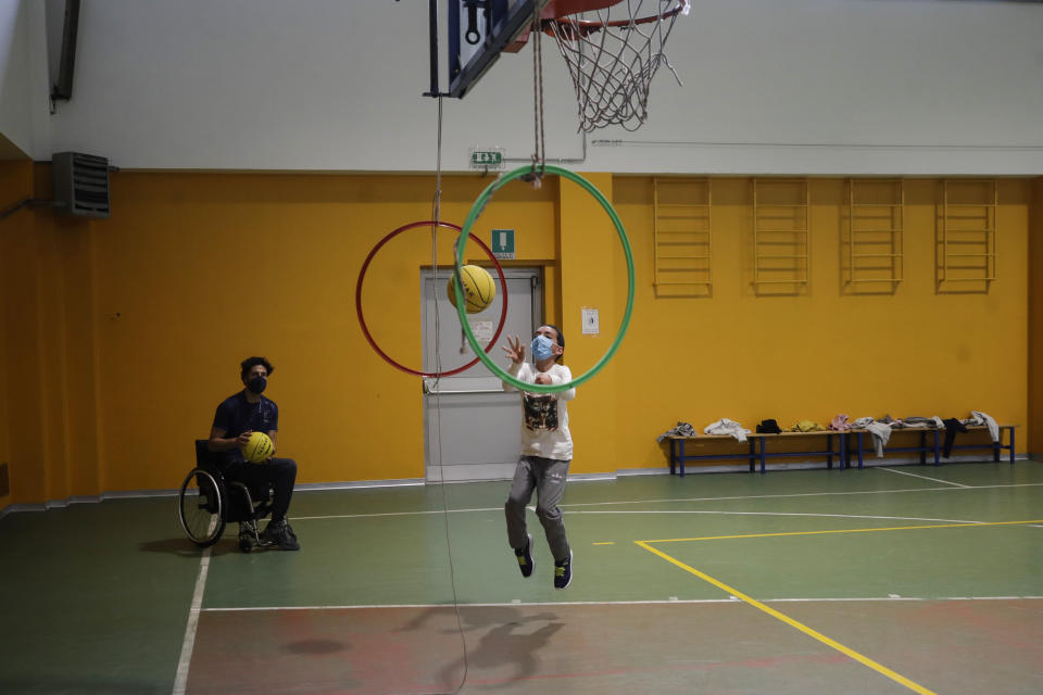 Adolfo Damian Berdun, of Argentina, a professional player and captain of the Argentine basketball Paralympic team, teaches children basketball at a primary school in Verano Brianza, outskirt of Milan, Italy, Tuesday, May 11, 2021. Four second-grade classes in the Milan suburb of Verano Brianza have been learning to play basketball this spring from a real pro. They also getting a lesson in diversity. Their basketball coach for the last month has been Adolfo Damian Berdun, an Argentinian-Italian wheelchair basketball champion. Berdun, 39, lost his left leg in a traffic accident at ag 13 in his native Buenos Aires, and he has visited many schools over the years to discuss how he has lived with his disability. (AP Photo/Luca Bruno)