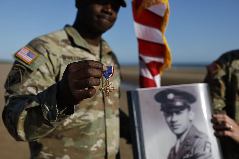 A soldier of the First U.S. Army shows the Distinguished Service Cross while another holds the portrait of of Waverly Woodson Jr., a medic who was part of the only Black combat unit to take part in the D-Day invasion of France during World War II, being posthumously awarded the Distinguished Service Cross in recognition of the heroism and determination he showed treating troops under heavy enemy fire , on Omaha Beach in Colleville-sur-Mer, France on Friday, June 7, 2024, (AP Photo/Jeremias Gonzalez)