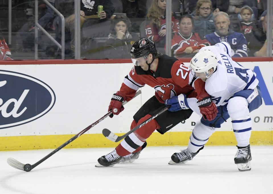 New Jersey Devils center Blake Coleman (20) controls the puck as he is checked by Toronto Maple Leafs defenseman Morgan Rielly (44) during the second period of an NHL hockey game Friday, Dec. 27, 2019, in Newark, N.J. (AP Photo/Bill Kostroun)