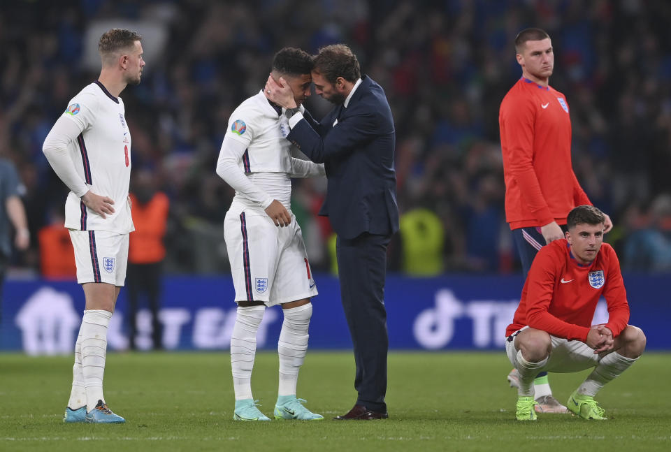 FILE - England's manager Gareth Southgate, center right, consoles England's Jadon Sancho after the penalty shootout of the Euro 2020 soccer final match between England and Italy at Wembley stadium in London, Sunday, July 11, 2021. Black players like Marcus Rashford and Bukayo Saka have flourished even after being targeted online for missing penalties in England's shootout loss to Italy in the European Championship final in 2020. But a third Black player who also missed a penalty and was racially abused, Jadon Sancho, has struggled on the field ever since. (Laurence Griffiths/Pool via AP, File)