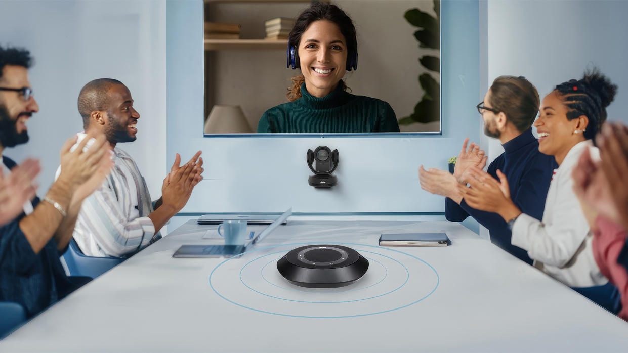  The new AVer camera and speaker videoconferencing solution being used in a medium-sized conference room with smiling people. . 