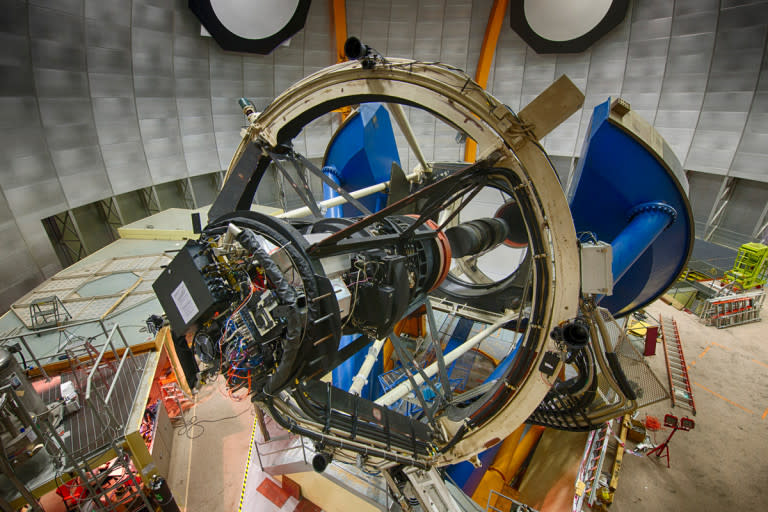 The Víctor M. Blanco 4-meter Telescope has a 4-meter (13-foot) diameter mirror, which weighs 15,400 kg (34,000 lbs). It was designed in the 1960s. The Dark Energy Camera (black paint) is mounted at the prime (first) focus near the top of the Serrurier truss (white paint). The blue-painted structure is the large bearing that allows the telescope to move in right ascension. The telescope declination axis is located at the level of the middle of the right ascension bearing and is best seen on the left side of the large U-shaped notch. The primary mirror is located a few feet lower than the declination axis.