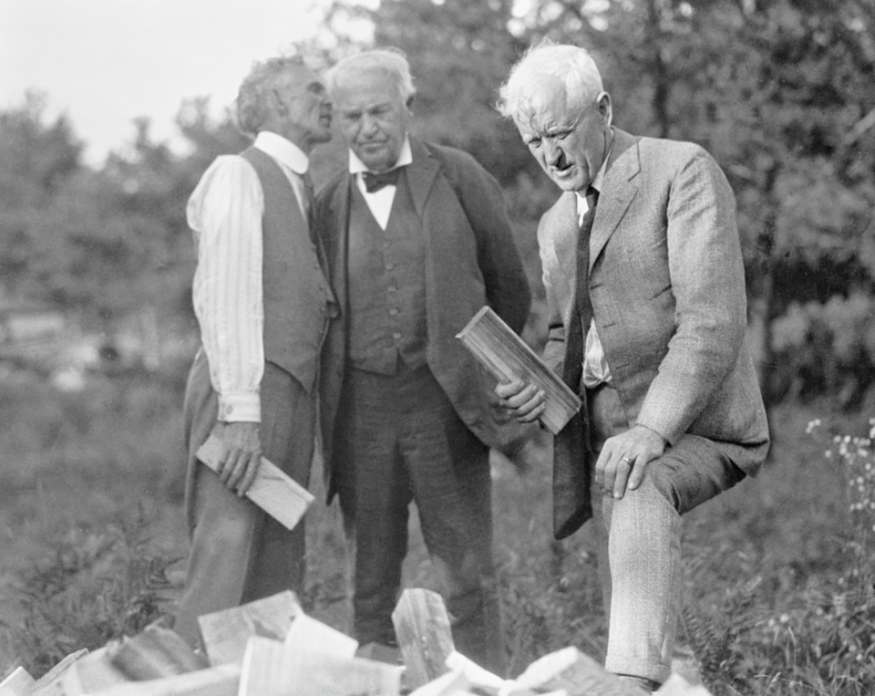 Henry Ford whispers in the ear of Thomas Edison as Edward Kingsford looks at a woodpile in August 1923, at Cowboy Lake grove in what would later become part of the city of Kingsford.