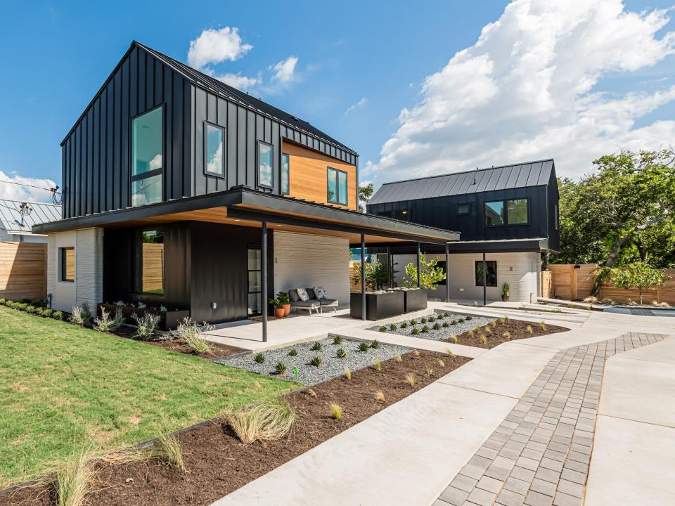 a walkway leading up to a row of 3D printed homes on a patch of grass