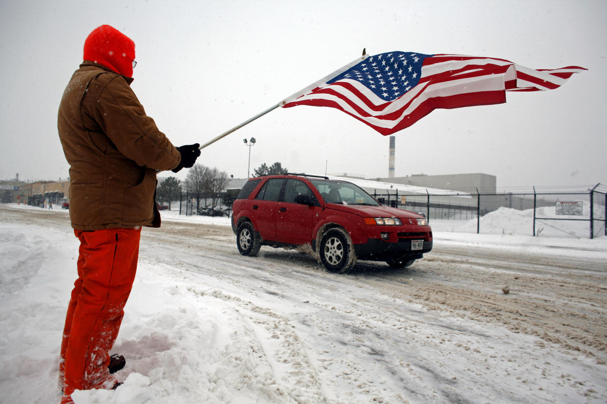 JANESVILLE, WI - DECEMBER 23:  Resident Billy Bob Grahn holds up a American Flag to show support as the remaining workers of the General Motors assembly plant leave after their final production line duties December 23, 2008 in Janesville Wisconsin. After more then 85 years of vehicle production, the Janesville plant closed after sending off its last Chevrolet and GMC SUVs, leaving more than 1200 employees with out jobs.  (Photo by Darren Hauck/Getty Images)