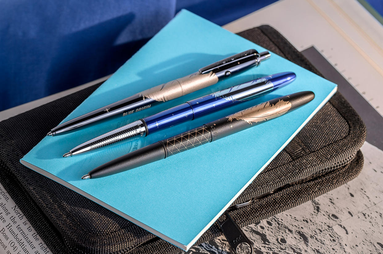  Three pens sit on a light-blue notebook on a table. 