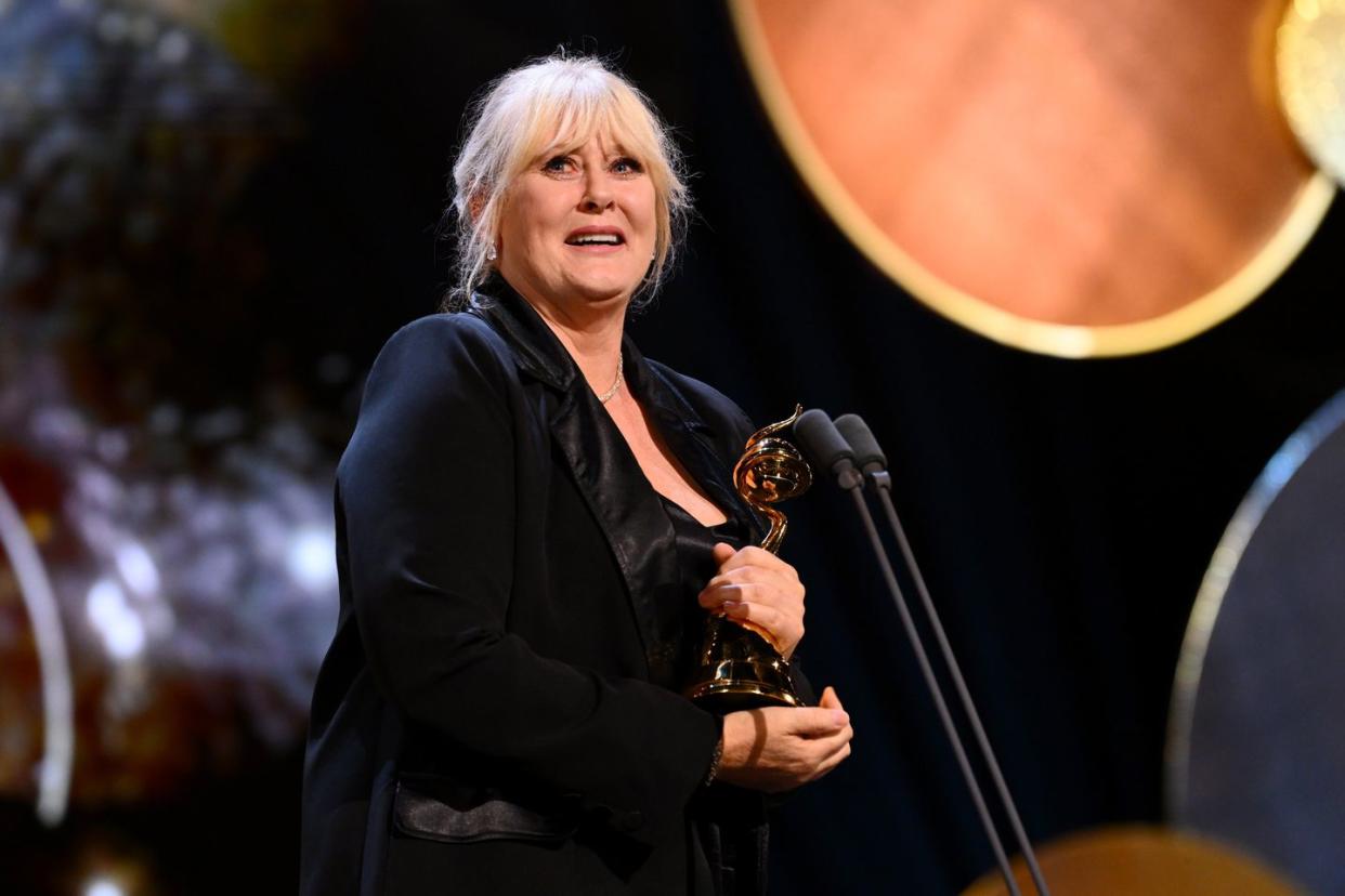 sarah lancashire smiles as she holds an nta awards trophy on stage