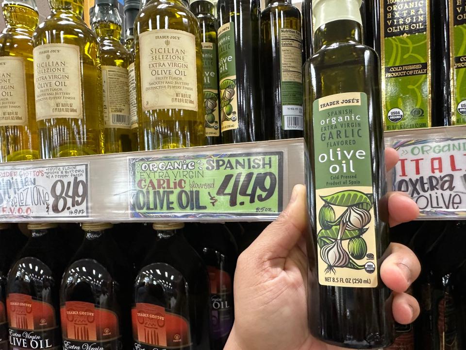 hand holding bottole of extra virgin olive oil in front of shelves of oil at trader joes
