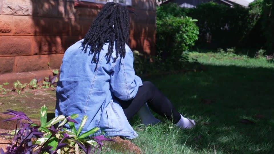 Ann, who fled Uganda, sits in the garden of the safe house in Kenya. She does not feel it's safe to venture further outside. - Fabien Muhire/CNN