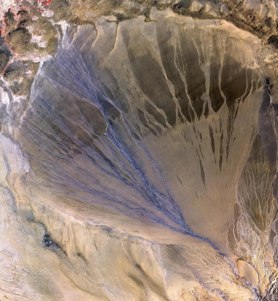 A vast alluvial fan blossoms across the desolate landscape between the Kunlun and Altun mountain ranges that form the southern border of the Taklimakan Desert in China&rsquo;s XinJiang Province. The left side is the active part of the fan, and appears blue from water currently flowing in the many small streams.