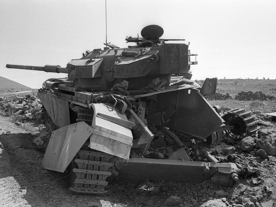 A black and white photo of a broken down tank on the side of the road on the Golan Heights during the Yom Kippur war.
