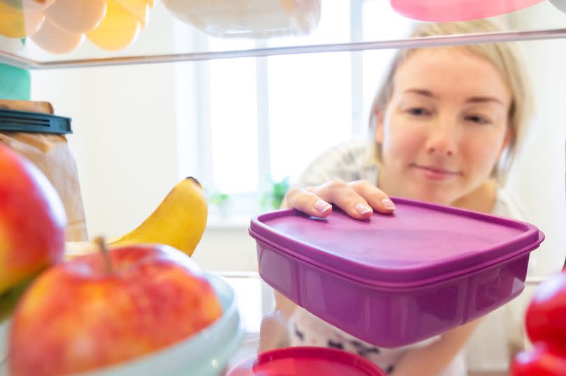 A woman putting food in a plastic container into her fridge