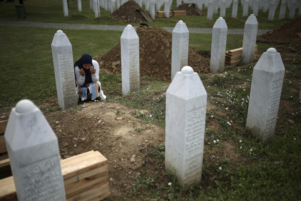 A woman prays near a grave of her family member in the Memorial centre in Potocari, Bosnia, Friday, July 8, 2022. After surviving the 1995 Srebrenica massacre in which over 8,000 of their male relatives were killed, women from the small town in eastern Bosnia dedicated the remaining years of their lives to the re-telling of their trauma to the World, honoring the victims and bringing those responsible for the killings to justice. (AP Photo/Armin Durgut)