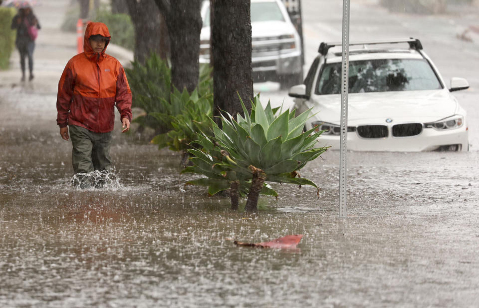 Person in raincoat walks through knee-high water on flooded sidewalk.  (Mario Tama / Getty Images)