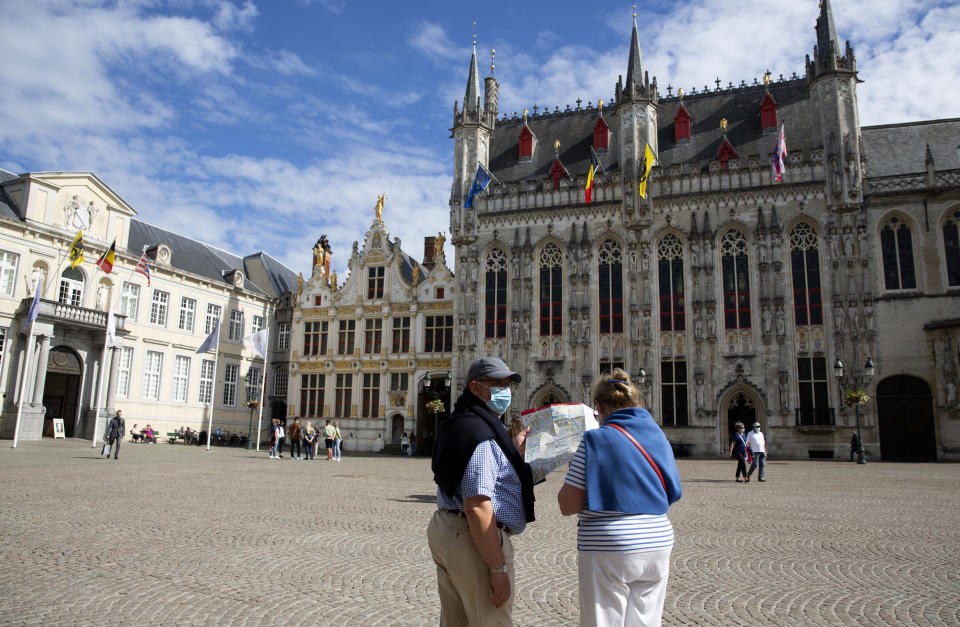 A couple in protective face masks consult a tourist map in the center of Bruges, Belgium, Monday, Aug. 24, 2020. Tourism sector losses have piled up in the tens of billions of euros across the 27-nation European Union, and the continent's vaunted government support and social security system is under increasing strain to prop up the sector. (AP Photo/Virginia Mayo)