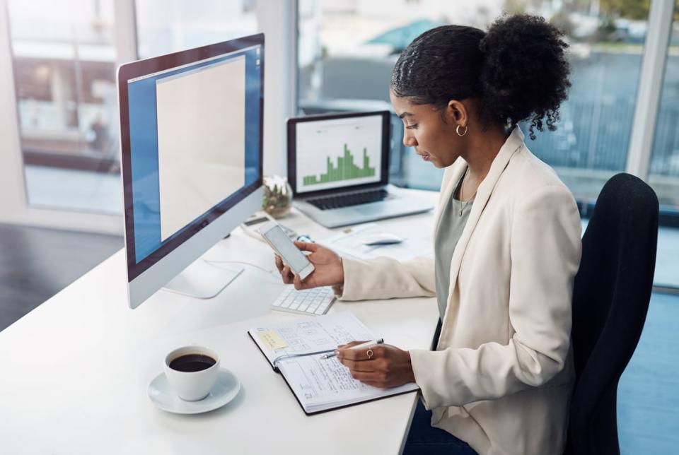 Person looking at a phone and two computers.