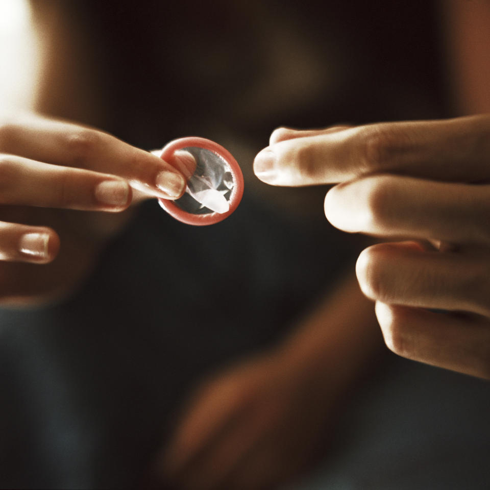 a close up of an unwrapped condom in front of people about to be intimate